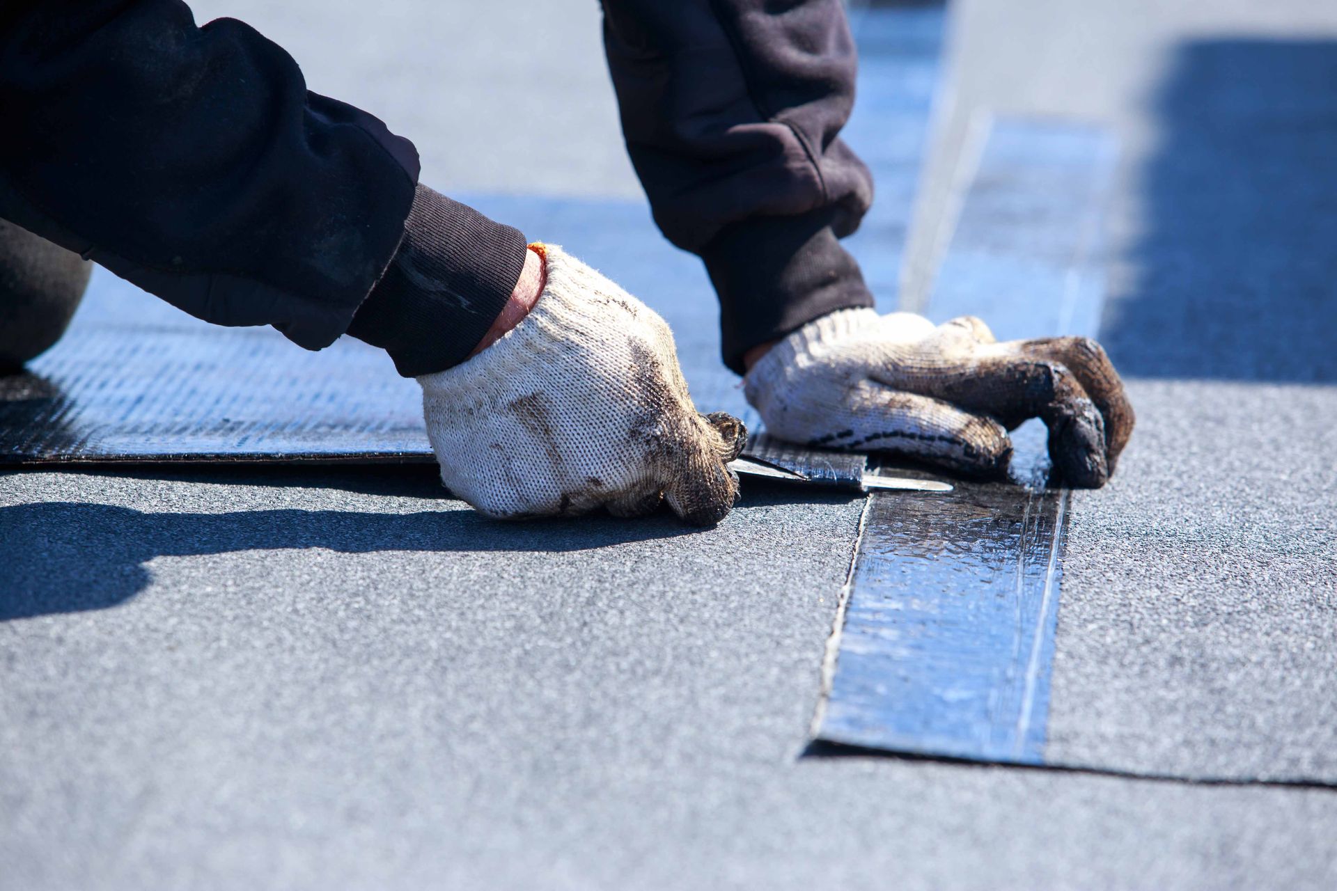 Person in work gloves installing a strip of sealant on a flat roof.