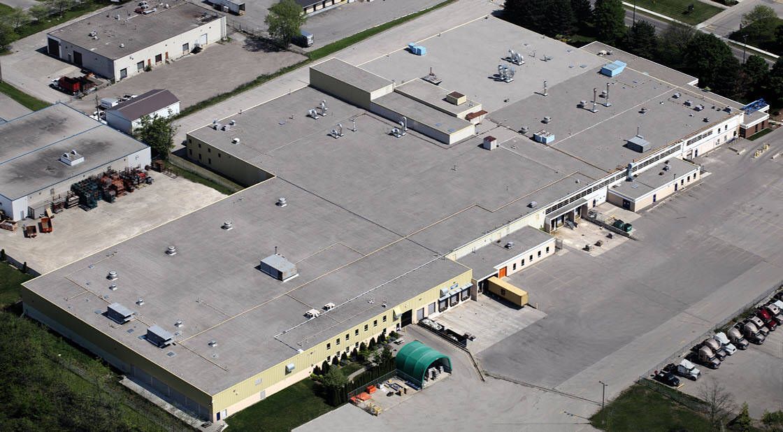 Aerial view of a large industrial building with a flat roof and surrounding parking lot and other structures.