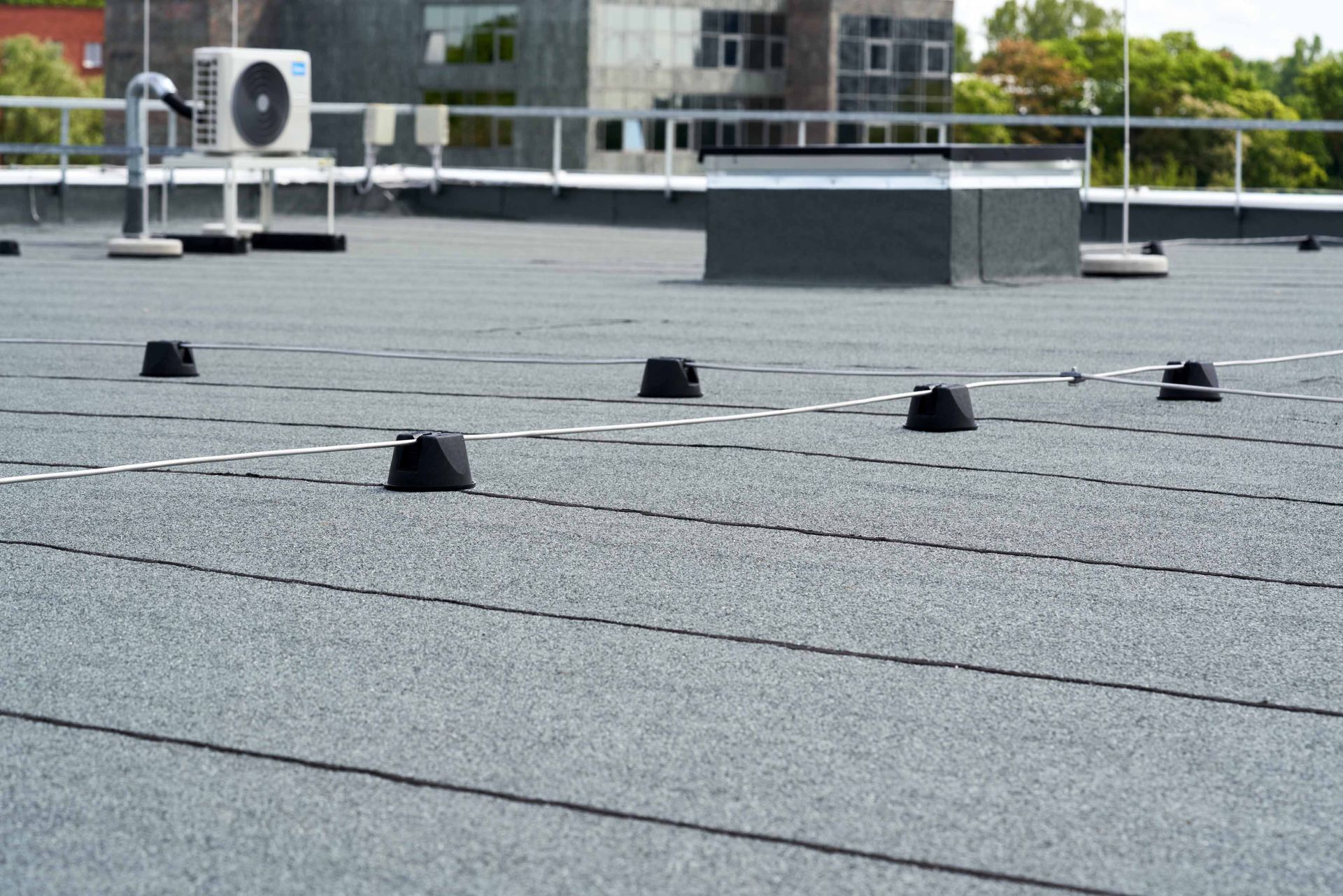 Flat rooftop with black surface and small black objects. Gray building in the background.