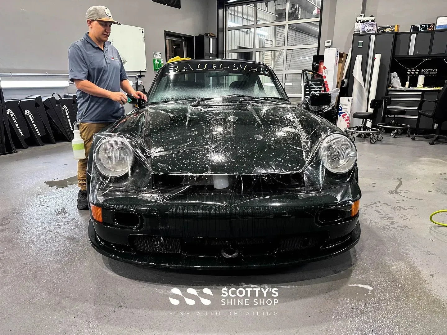 Black sports car being washed in a garage, with a person standing beside it.