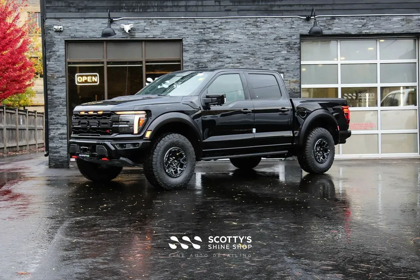 Black lifted pickup truck parked on a wet lot outside a garage.