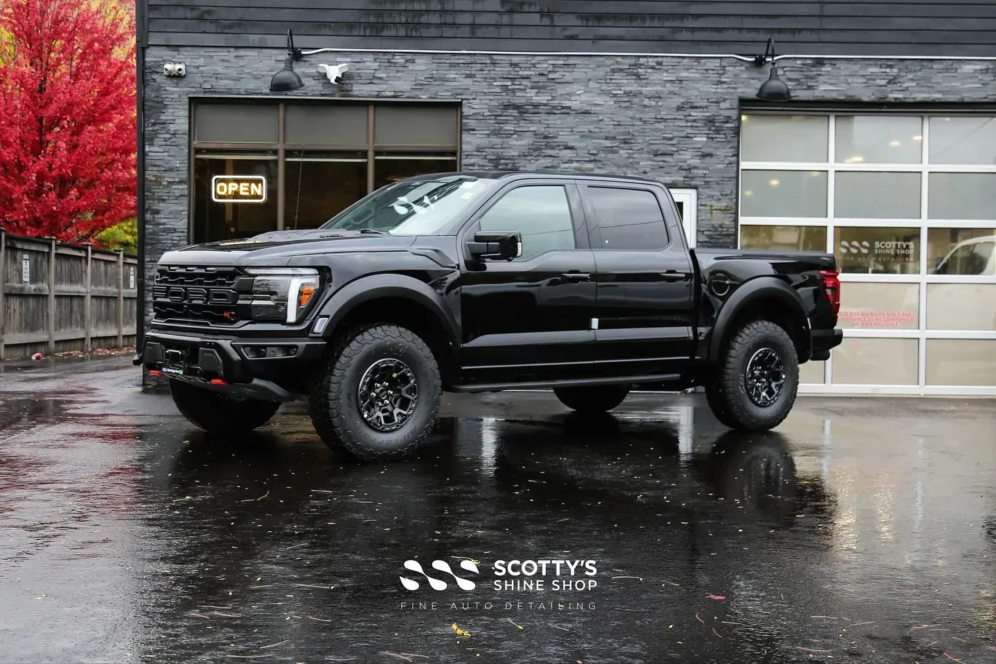 Black lifted pickup truck parked on wet pavement outside a gray building