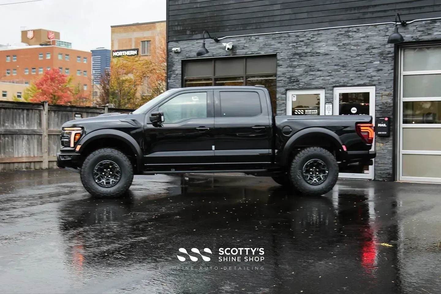 Black pickup truck parked on wet pavement outside a building with glass doors.