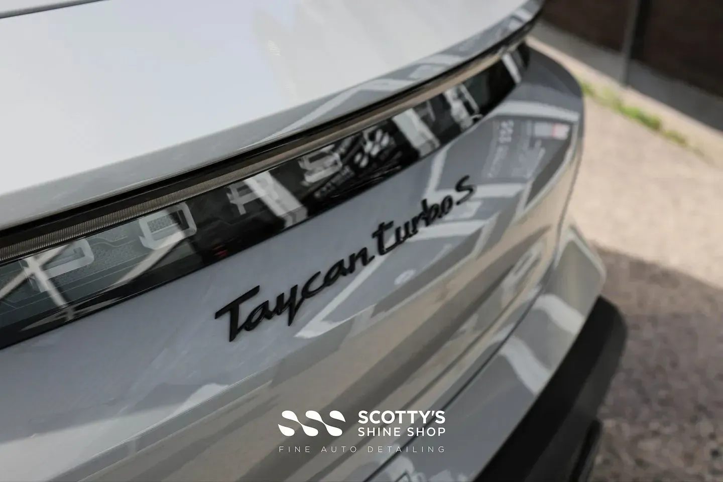 Close-up of a silver Porsche Taycan Turbo S rear badge and taillight on a driveway