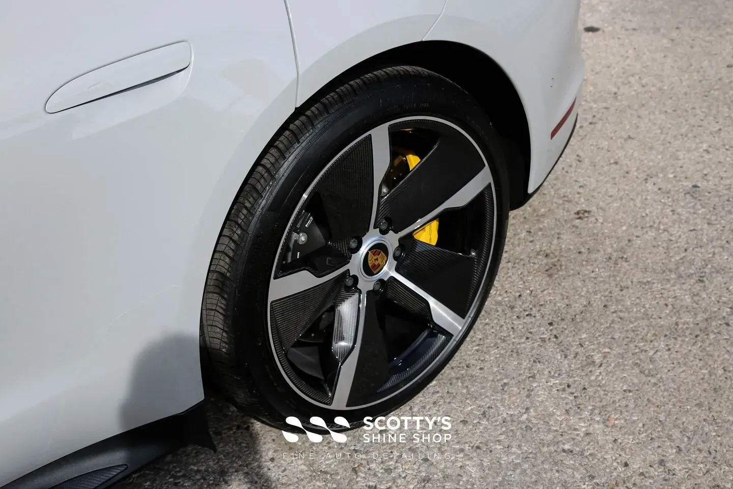 Close-up of a white car’s rear wheel with black five-spoke rim and yellow brake caliper.