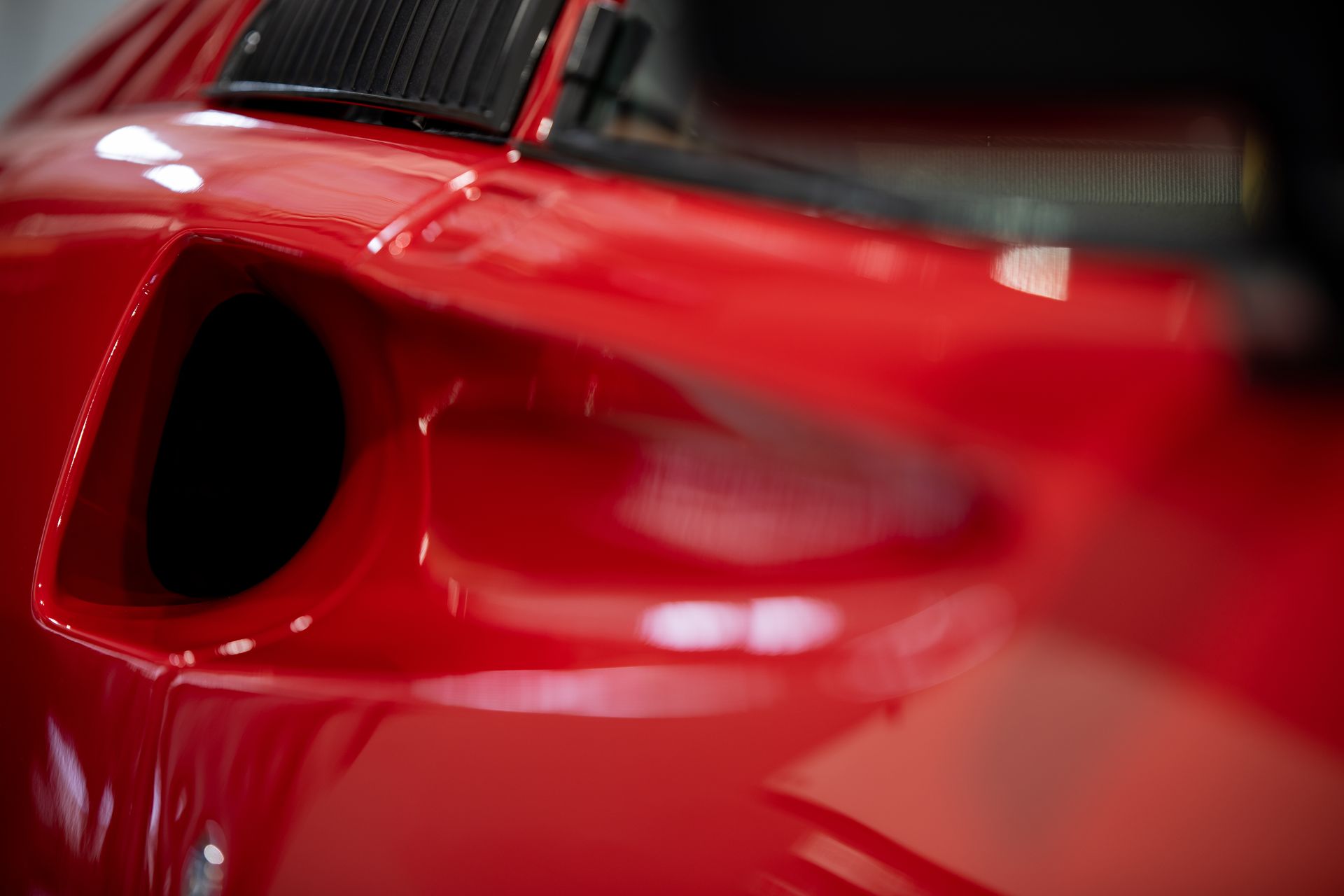 Close-up of a glossy red sports car body with a black side air intake