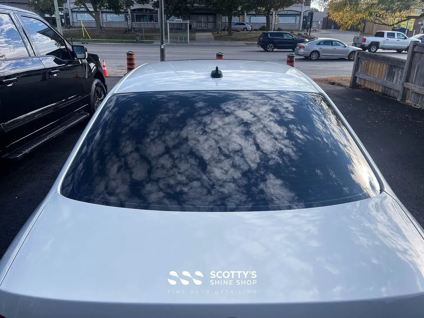 White car seen from above in a parking lot with reflections on the rear window and Scott’s logo on the trunk