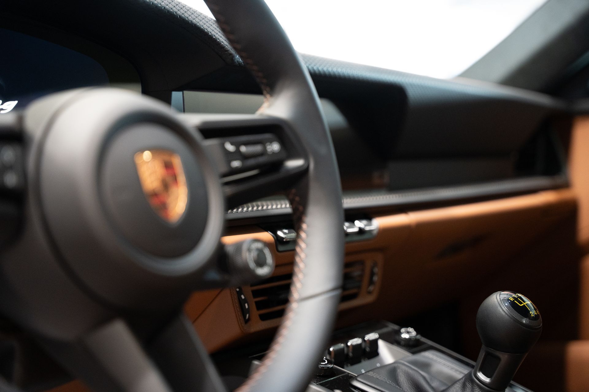 Close-up of a Porsche car interior with steering wheel, dashboard, and manual gear shift