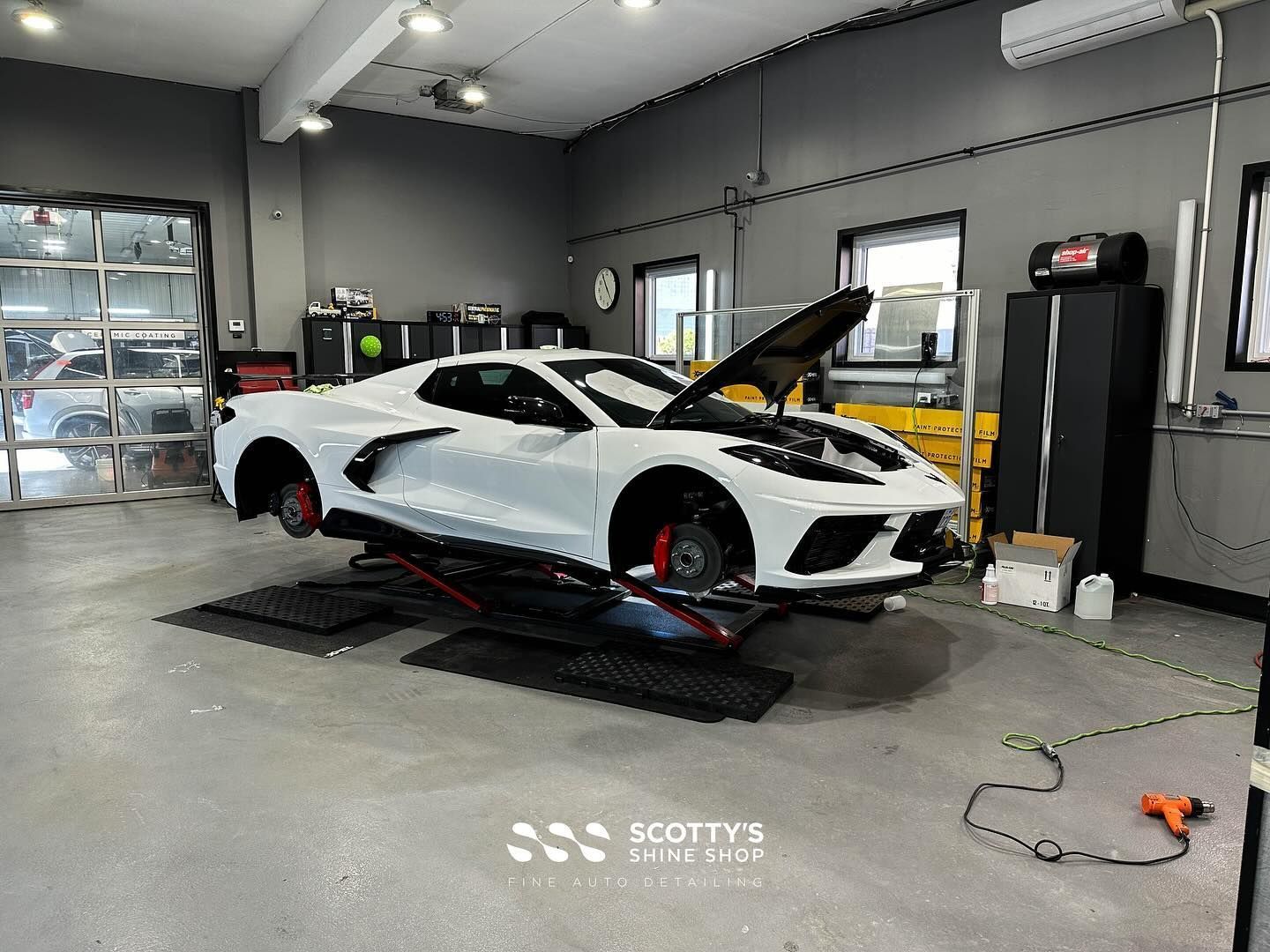 White sports car on a garage dynamometer with its hood open, inside a workshop