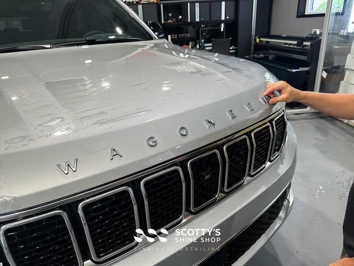 Close-up of a silver Wagoneer hood emblem being applied in a garage