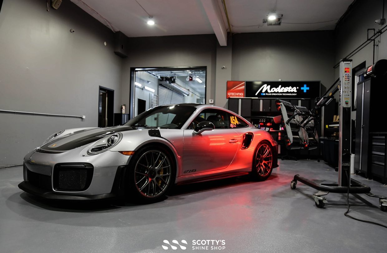Silver sports car with red lighting in a garage, on a shop floor with equipment nearby