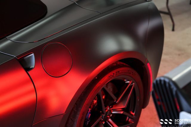 Glossy black sports car rear quarter with red underglow lighting and black alloy wheel
