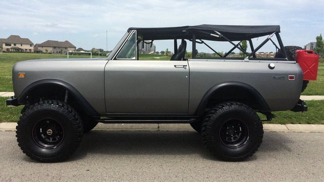 Gray vintage off-road SUV with black soft top, parked in profile on a street.