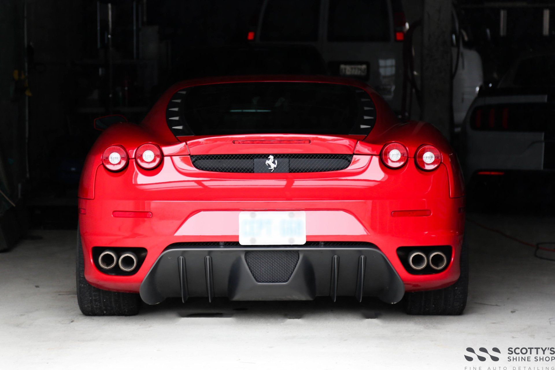 Red Ferrari sports car rear view in a garage, with quad exhausts and black diffuser