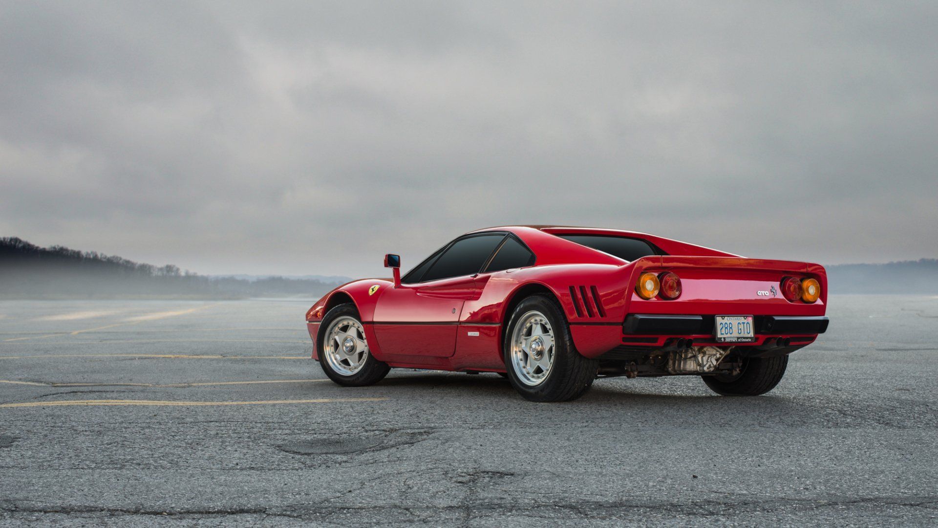 Red sports car parked on a wet road in a misty, overcast landscape