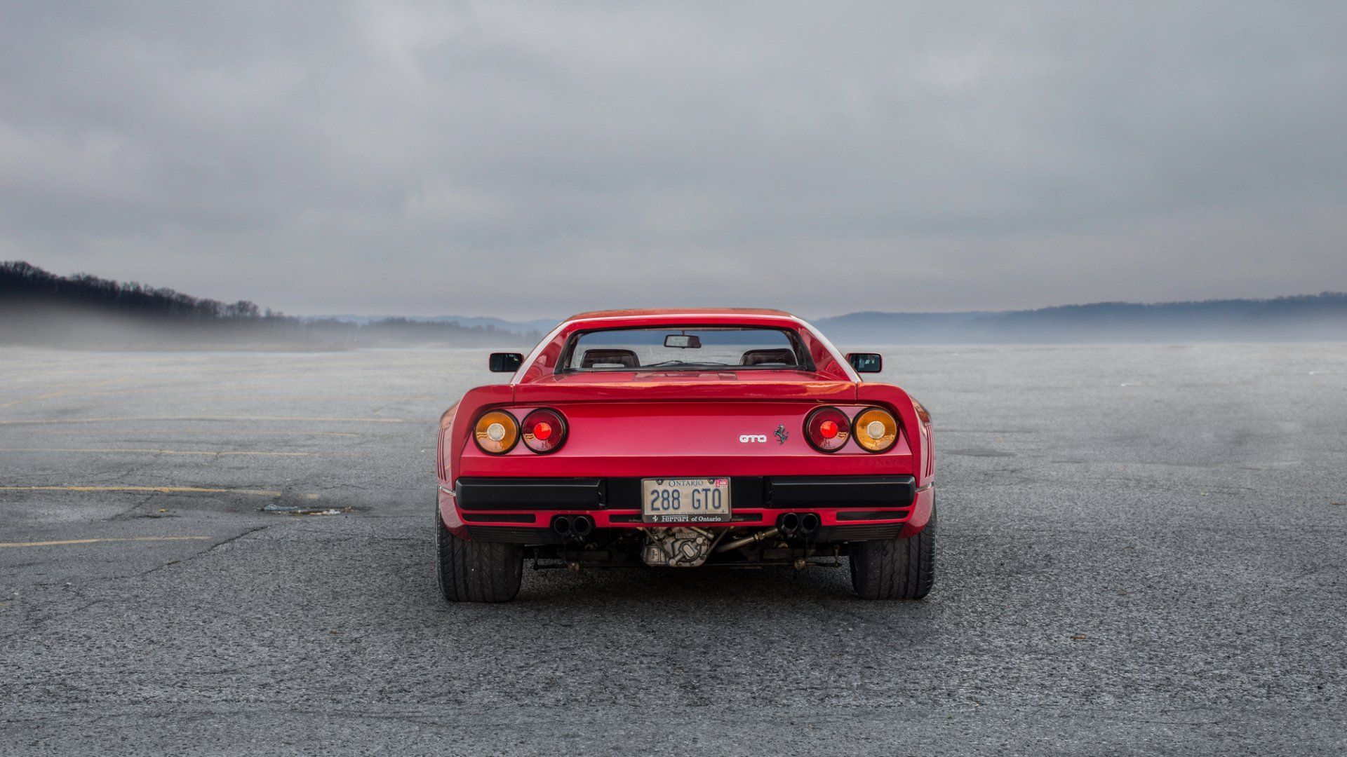 Red sports car seen from behind on a wet, empty road under a gray sky