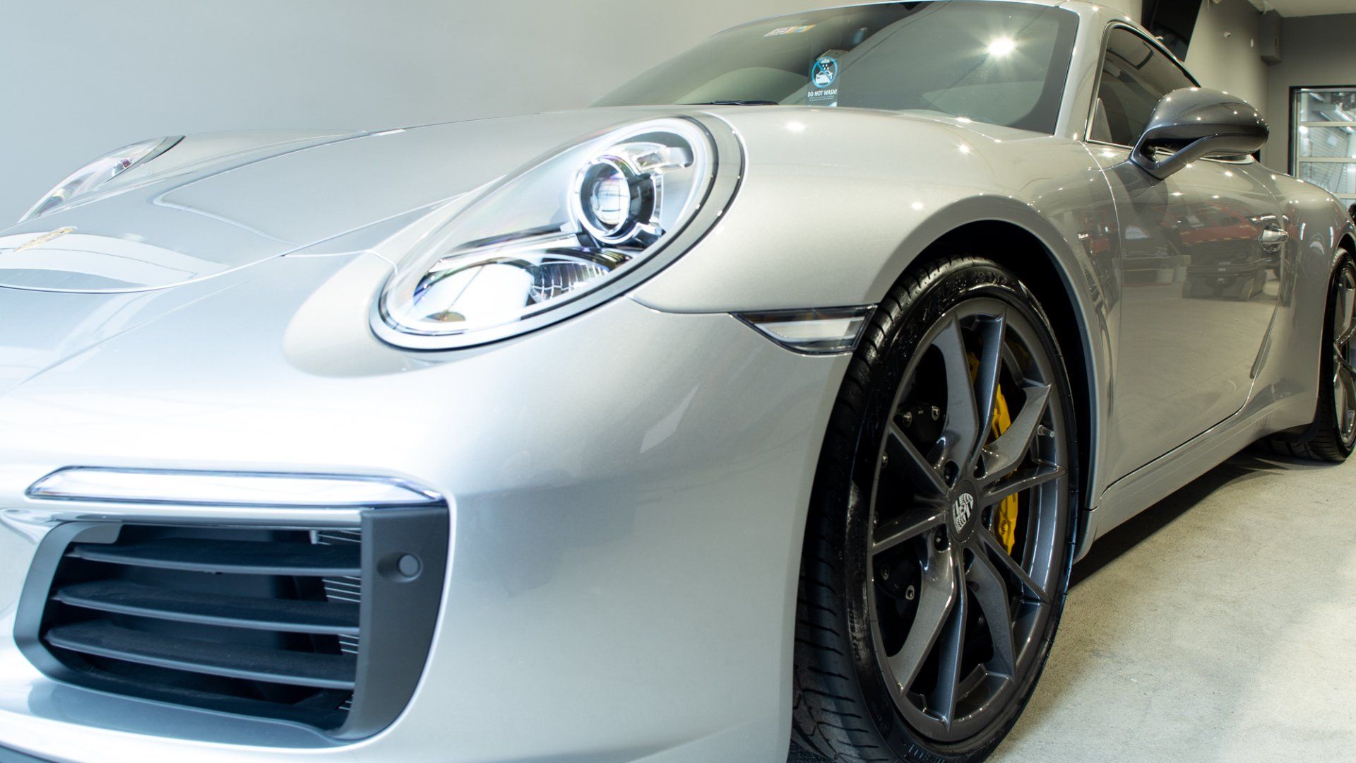 Silver sports car parked indoors, front-left view with sleek headlights and black wheels