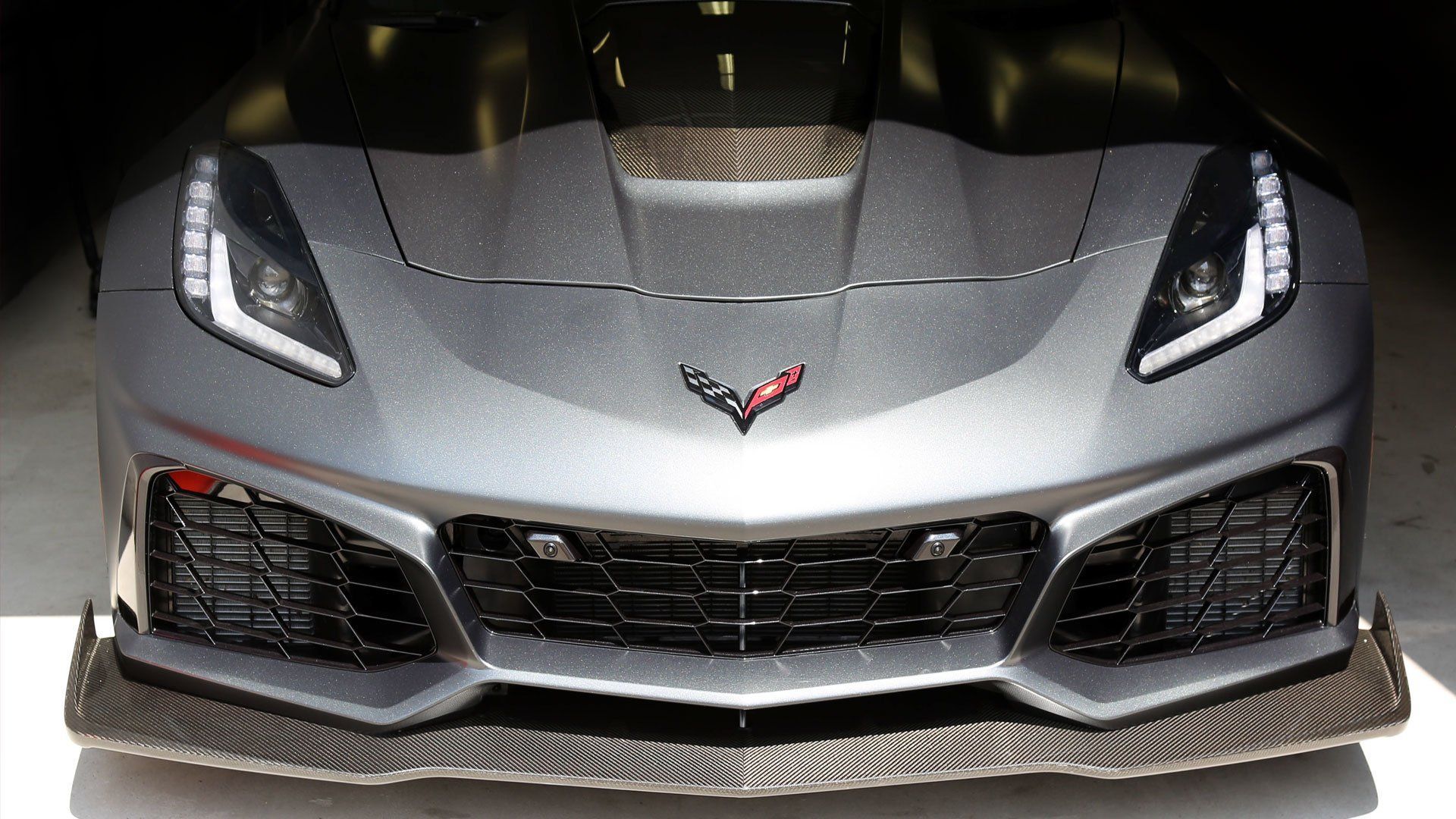 Front view of a silver Chevrolet Corvette sports car in a showroom, with hood and grille details visible