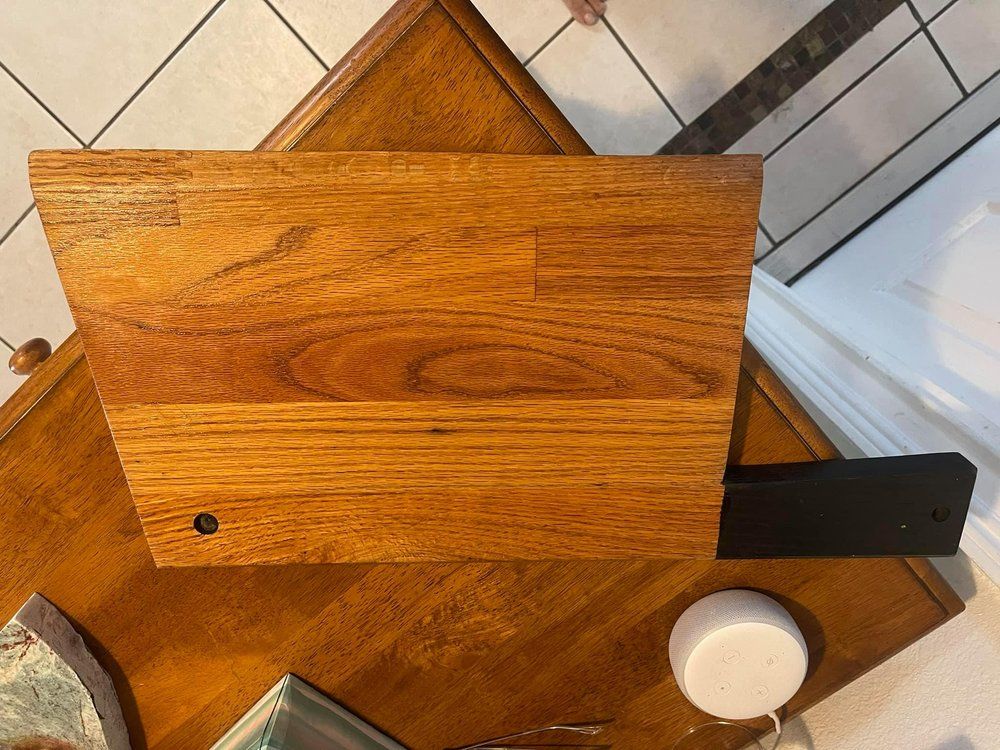 Wooden cutting board on a tiled countertop with a knife handle, bowl, and jar nearby.