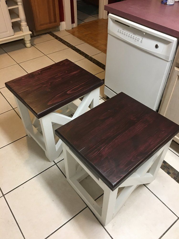 Two small dark-wood stools on a cream-tiled kitchen floor next to a white appliance