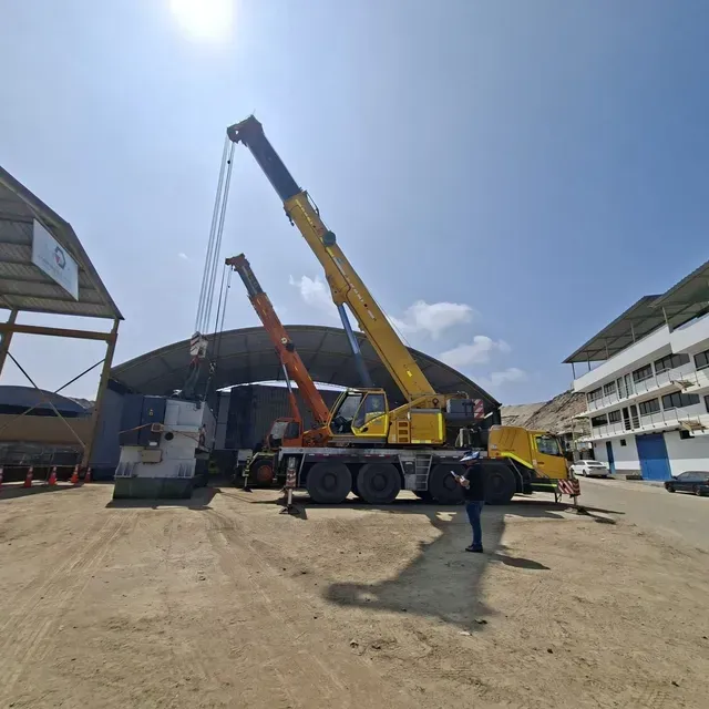 Dos grúas levantando una sección del techo en una obra de construcción bajo un cielo azul brillante.