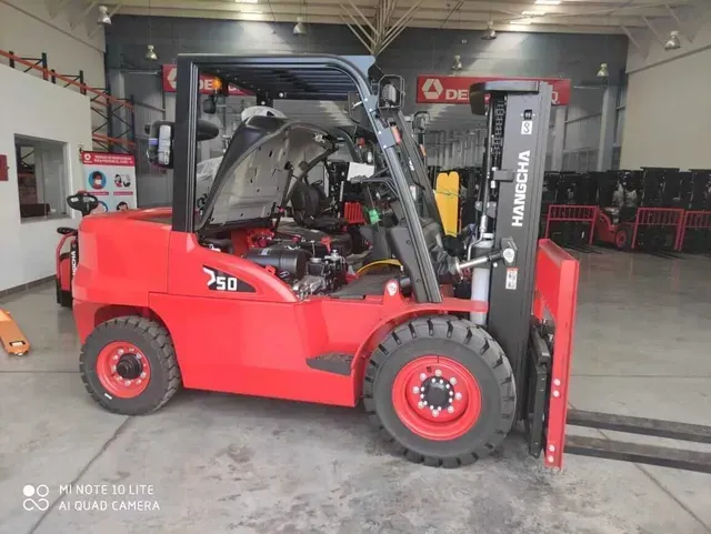 Carretilla elevadora roja en un taller mecánico, vista lateral con mástil elevado y cabina visible.
