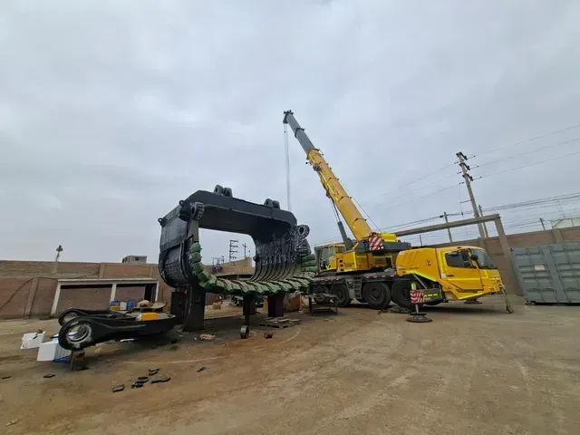 Grúa amarilla levantando equipo pesado en un patio industrial bajo un cielo nublado.