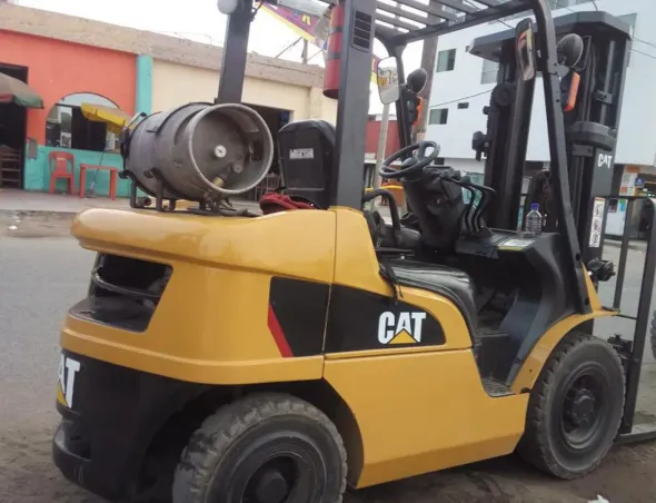 Una carretilla elevadora CAT amarilla con un tanque de propano estacionada al aire libre frente a un edificio.