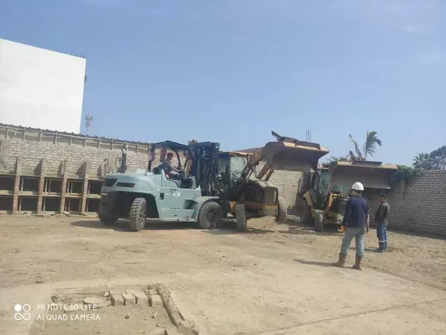 Un camión de construcción carga escombros en un patio polvoriento con trabajadores cerca.