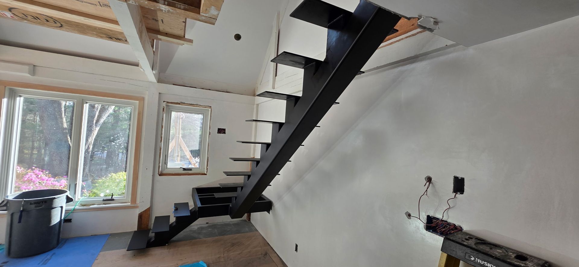 Bright interior with a floating black staircase, large windows, and a slanted white wall