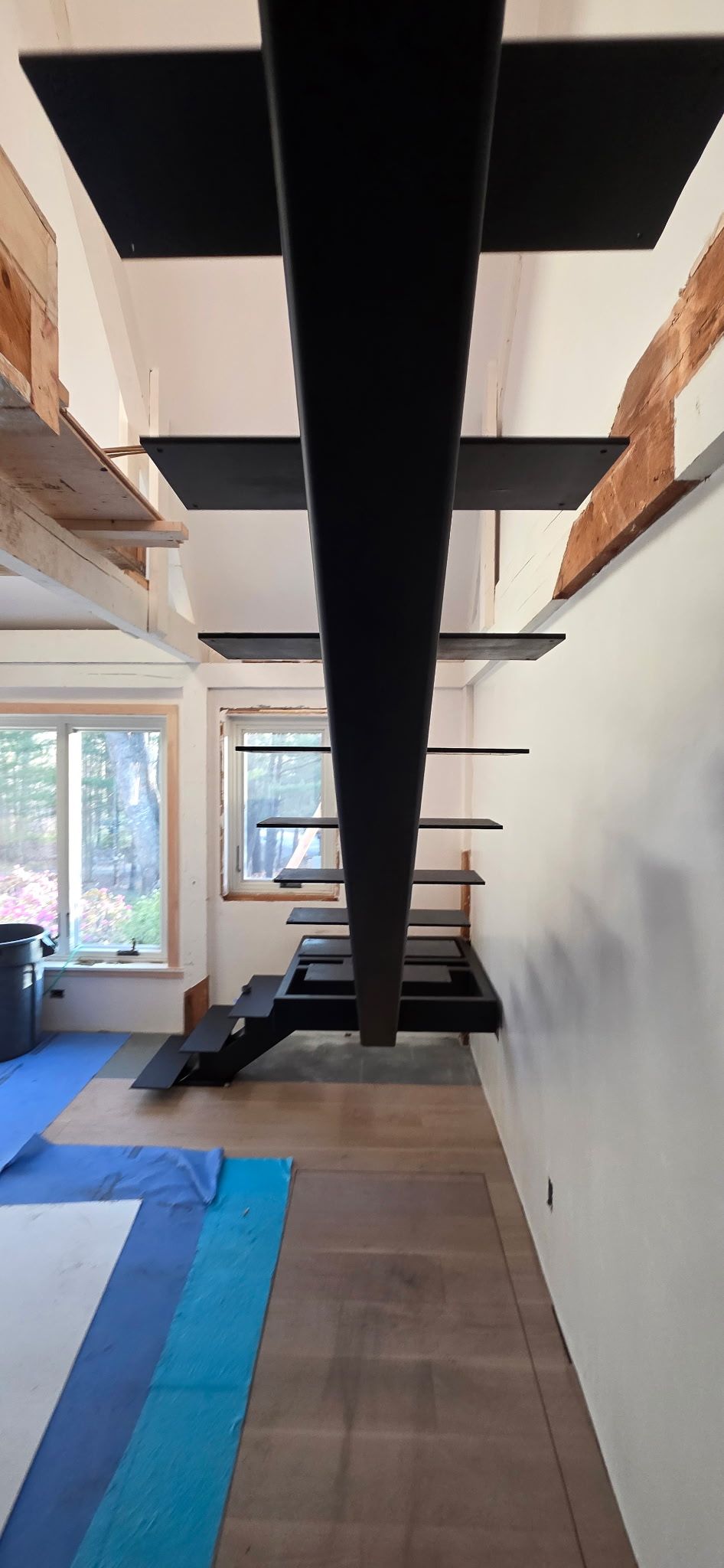 Modern interior with a black suspended staircase and mezzanine, viewed from below in a bright room