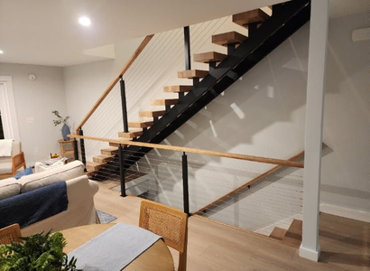 Elevated wooden deck with cable railing, orange wood posts, overlooking a forested area and parking lot below - NRK Welding LLC