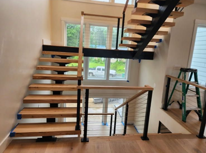 Elevated wooden deck with cable railing, orange wood posts, overlooking a forested area and parking lot below - NRK Welding LLC
