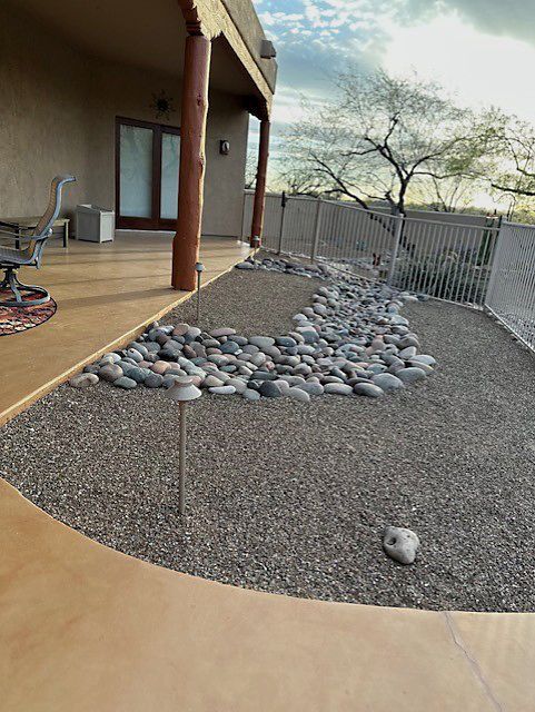 Patio with gravel landscaping and a line of rocks, fence, and tree in the background.