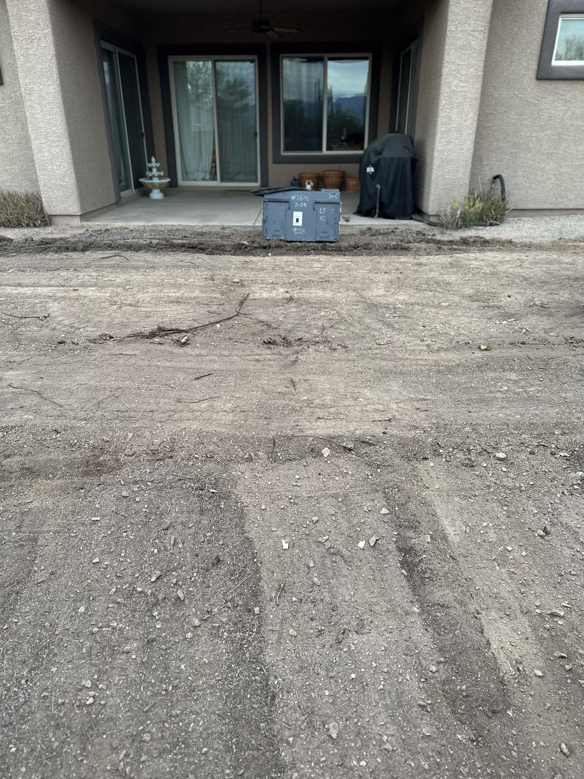 Gravel yard in front of a patio with a storage box and grill visible.