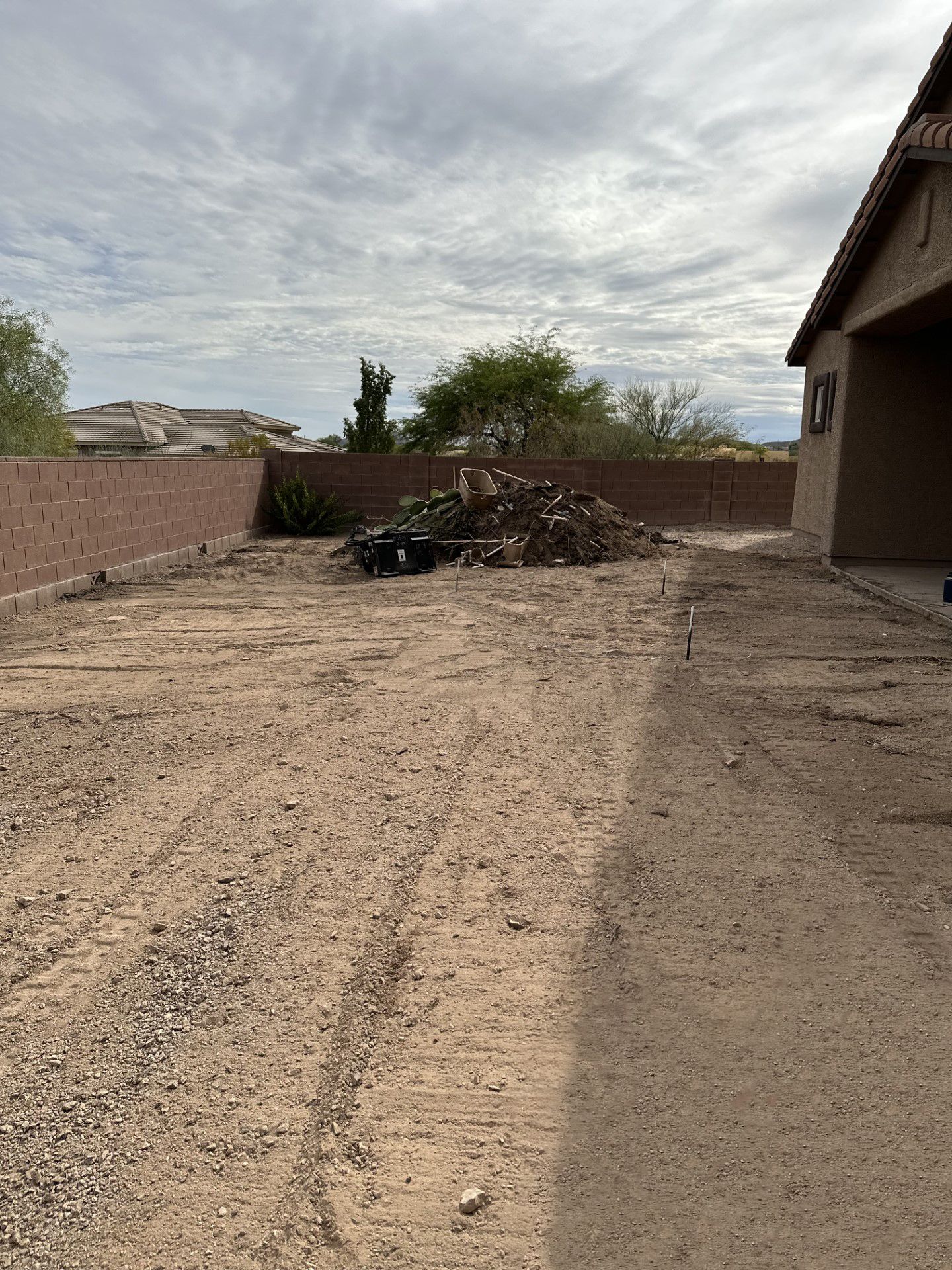 Dirt backyard with brown walls and a pile of debris under a cloudy sky.
