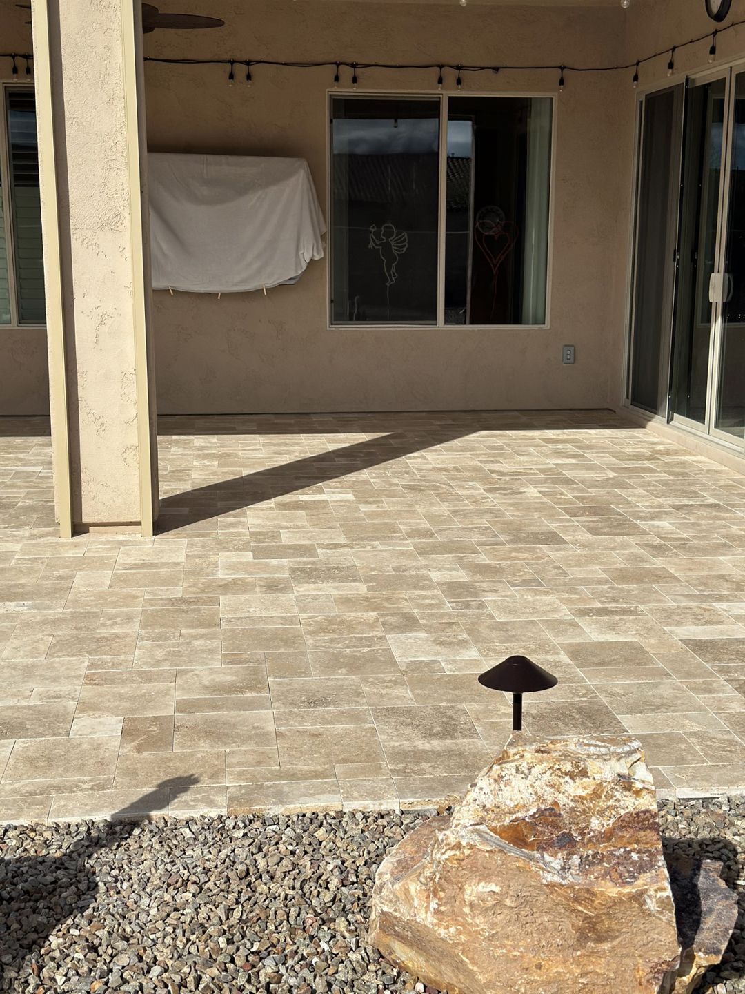Patio with stone pavers, a rock, and a landscape light. A covered window and a support column are also visible.