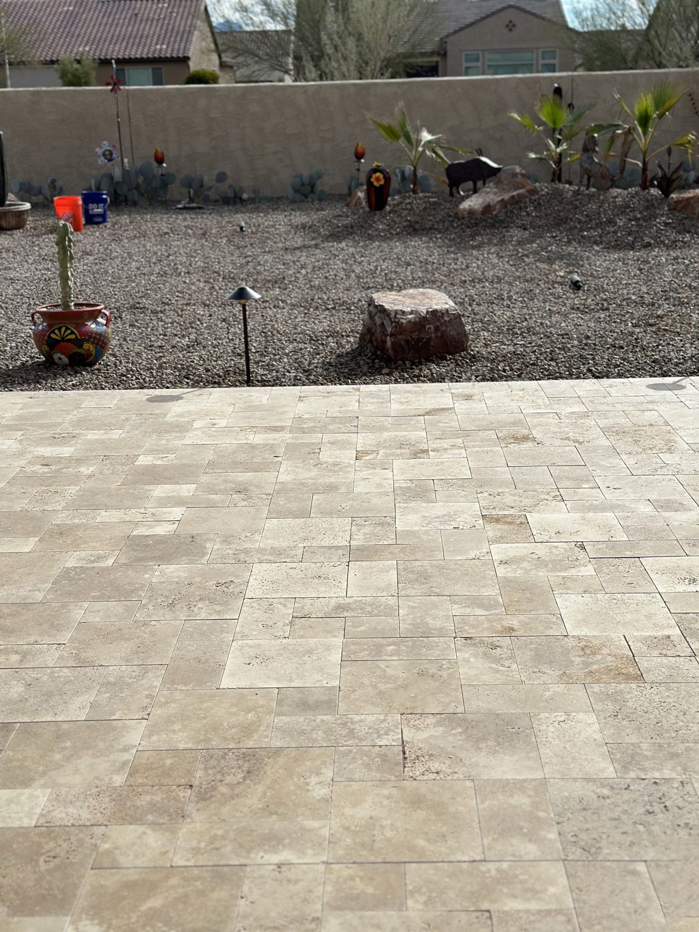 Stone patio leading to a gravel yard with potted plants and a decorative wall.
