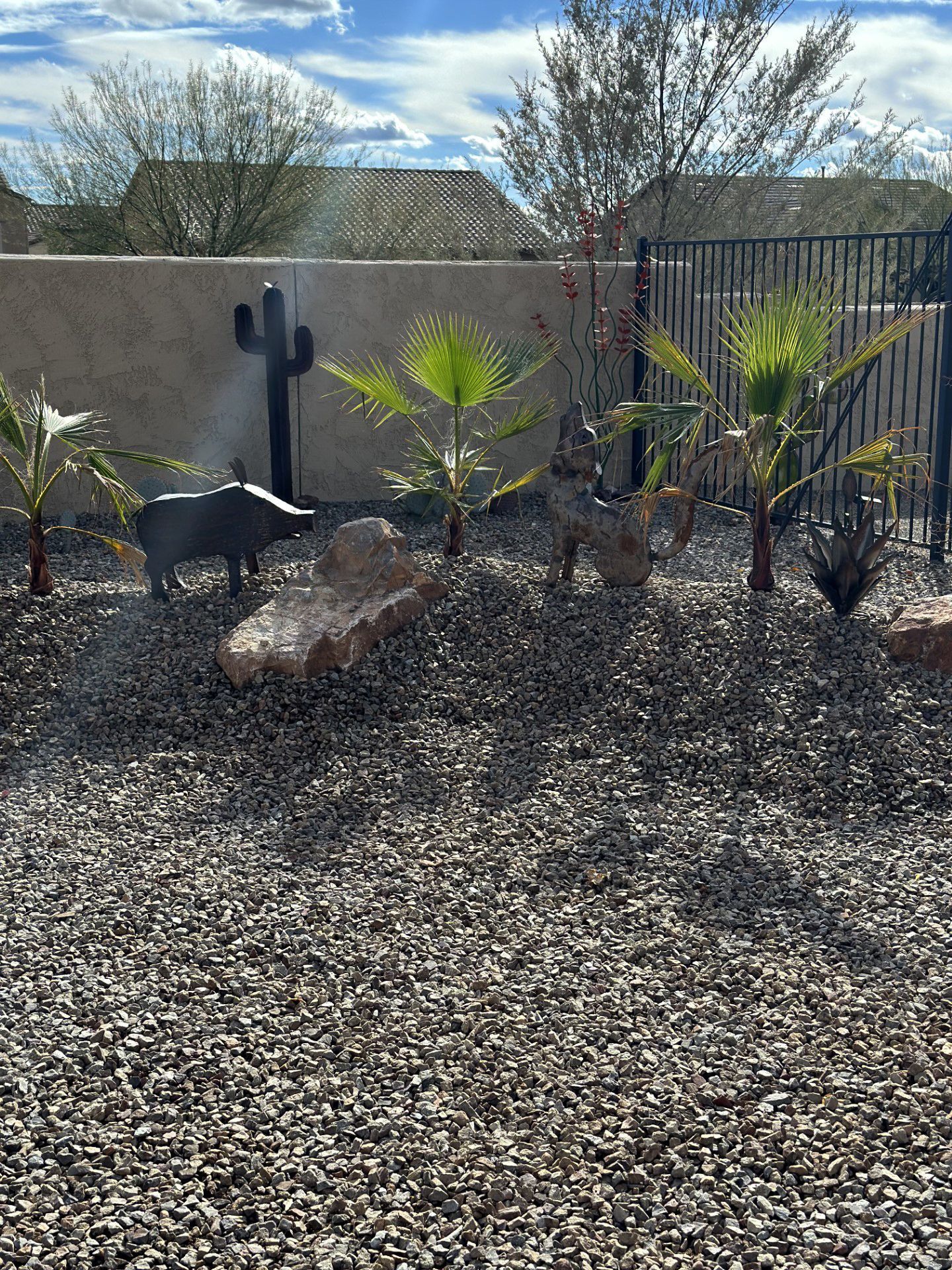 Desert landscape with palm trees, rock, metal animals, and a fence.
