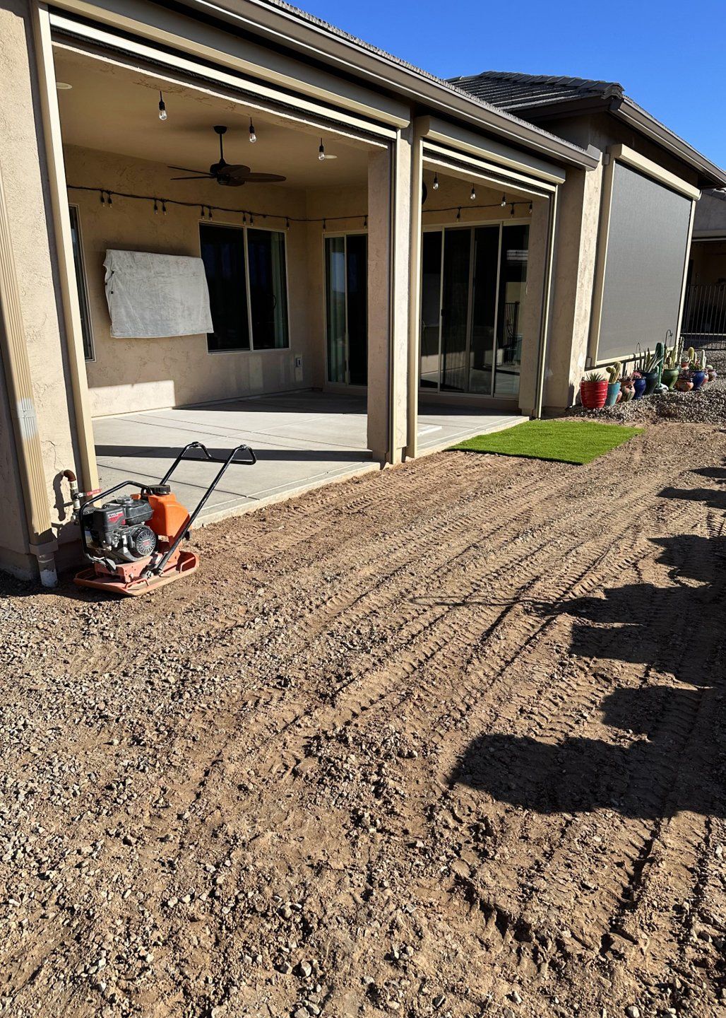Backyard with a patio, gravel path, and small grass section; a compactor sits on the gravel.