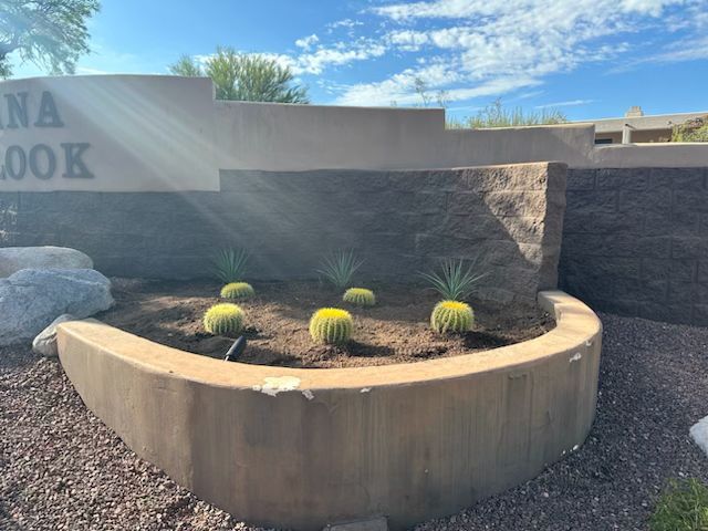 Sign for Arizona Brook with cacti in a curved planter bed under a blue sky.