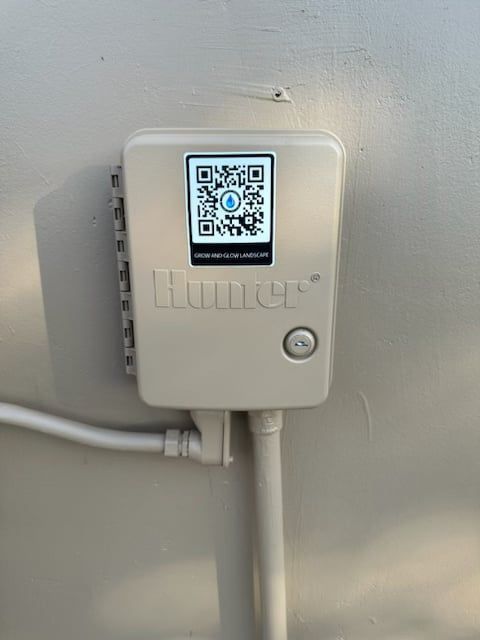 White Hunter irrigation controller mounted on a wall with a QR code displayed.