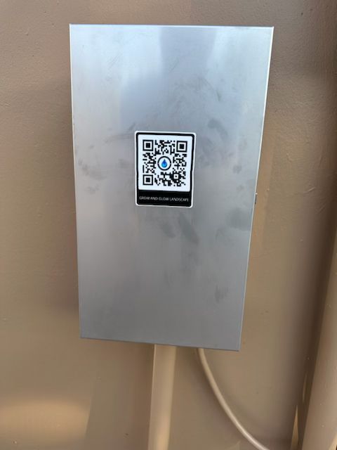 A metal box with a QR code sticker on a wall. A white cable runs from the bottom.