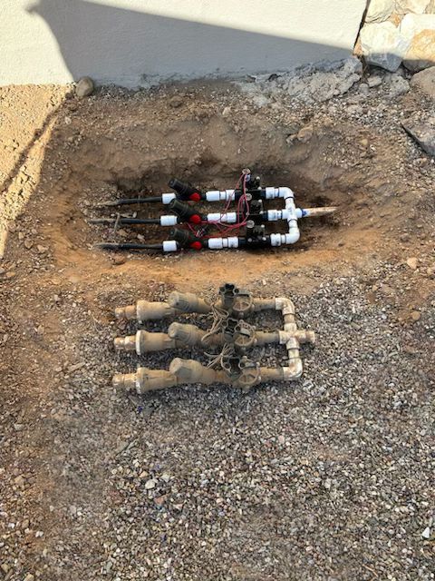 Two irrigation valve manifolds in a dirt pit. One is new and the other is old, dirty.