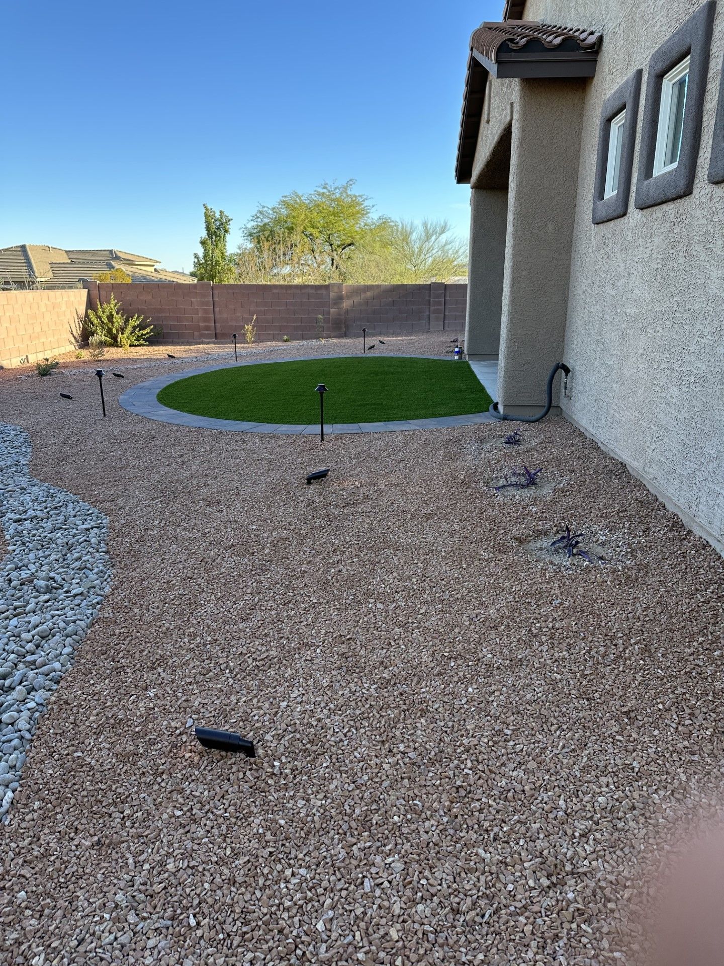 Backyard with gravel ground cover, a circular grass patch, and a house with a stucco exterior.