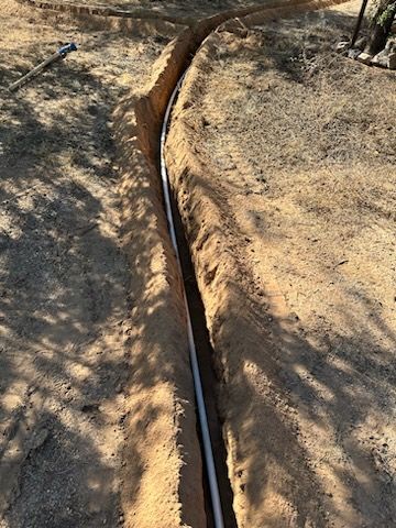A trench in dirt with a white pipe running through it, outdoors.