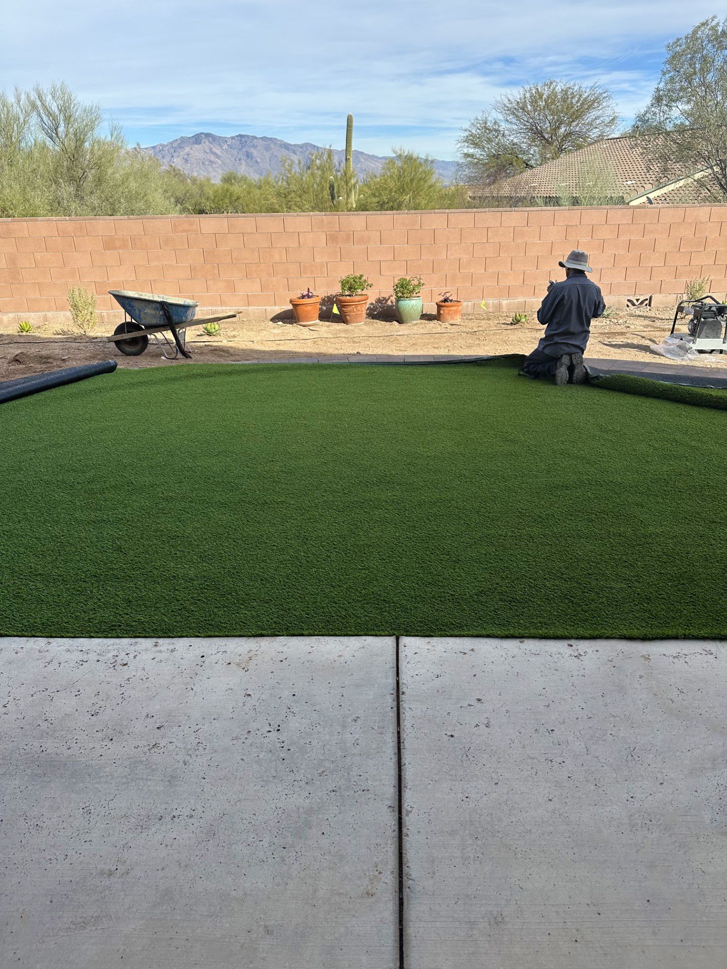 Person installing artificial turf in a backyard with a desert mountain backdrop.