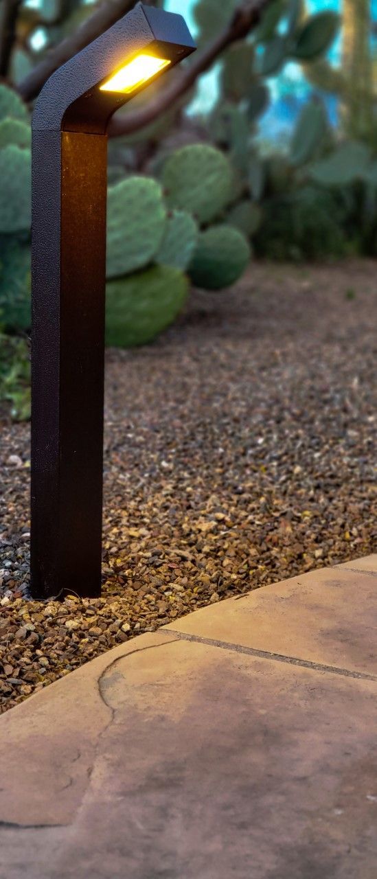 A black outdoor lamp illuminates a gravel bed and concrete walkway; cactus in the background.