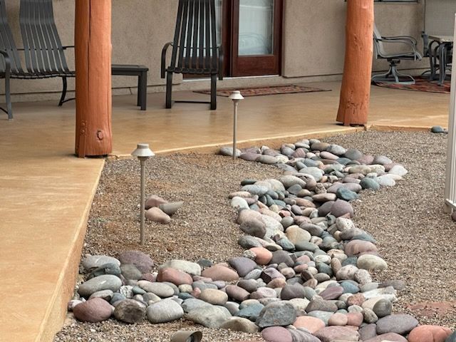 A gravel landscaping bed with a dry riverbed of rocks, illuminated by path lights, next to a porch.