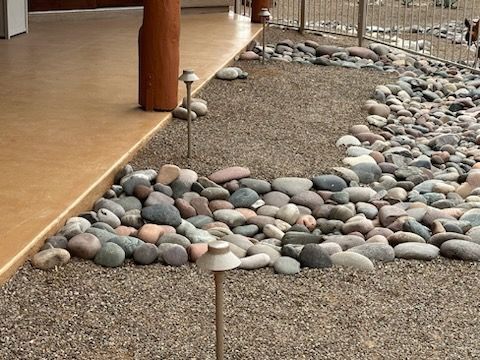 A gravel and rock landscaped yard with pathway lights next to a porch with a brown pillar.